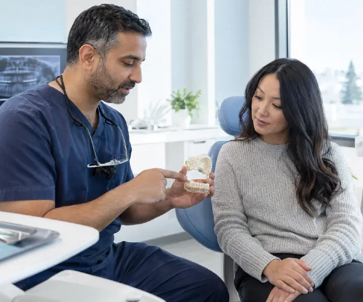 Dentist explaining surgical extraction anatomy on a jaw model to an adult patient