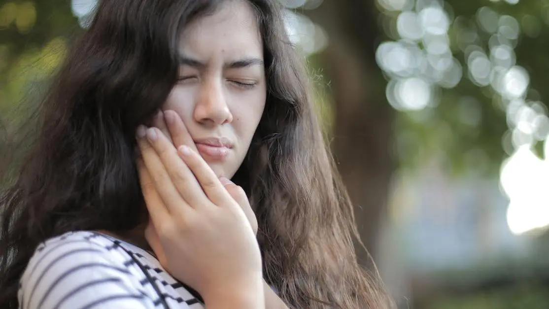 Young woman outdoors showing discomfort with toothache, highlighting dry socket symptoms.