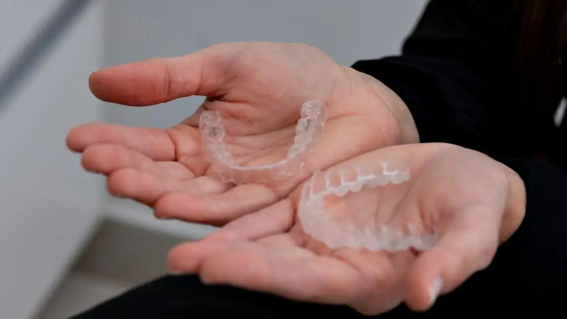 Ceramic braces vs Invisalign: hands holding clear aligners in a dental clinic.