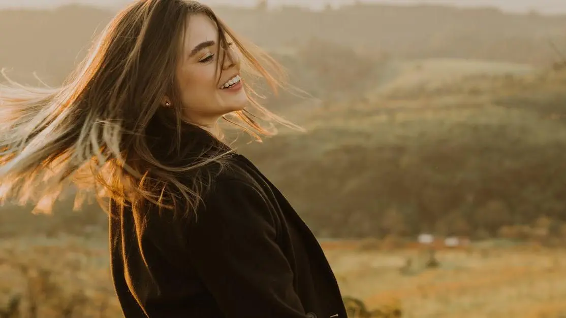 Happy woman with brown hair wearing Implant-supported dentures, smiling in a rural landscape.