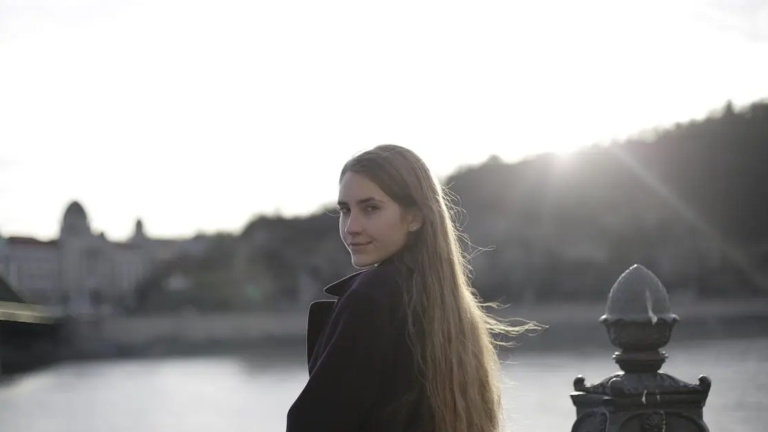 Smiling woman by waterfront at sunset, relevant to teeth whitening near Cookstown.