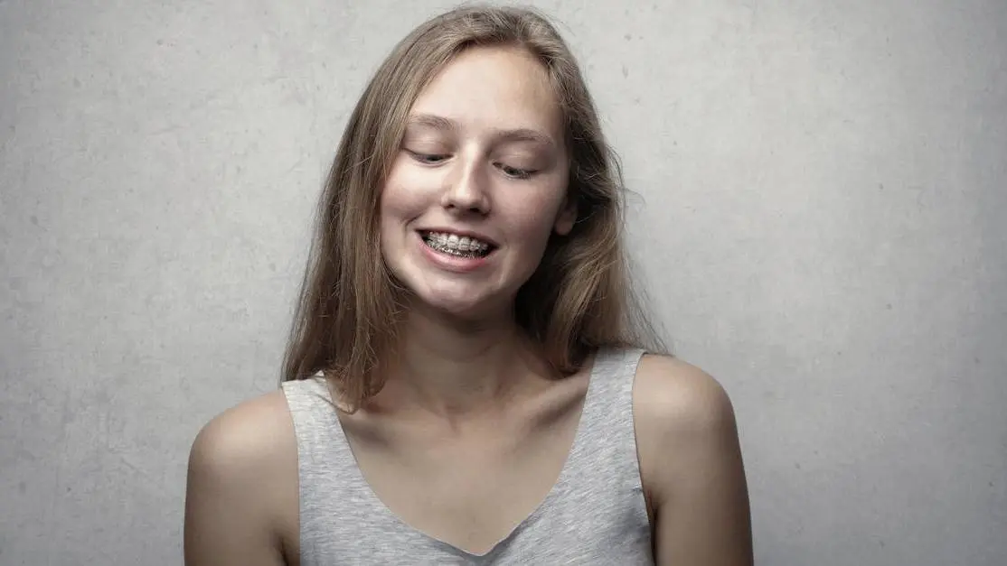 Young woman smiling with braces, highlighting Braces vs Invisalign in Thornton comparison.